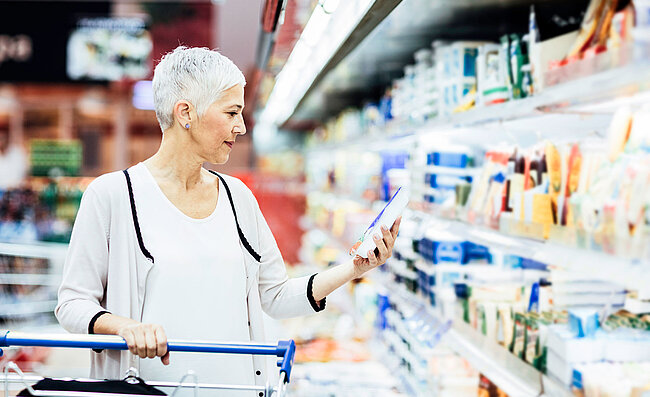 Žena stojí v supermarketu před oddělením s chlazeným zbožím